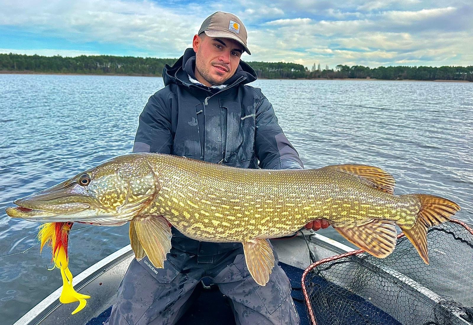 Pêcheur en bateau présentant un gros brochet pris sur un lac landais