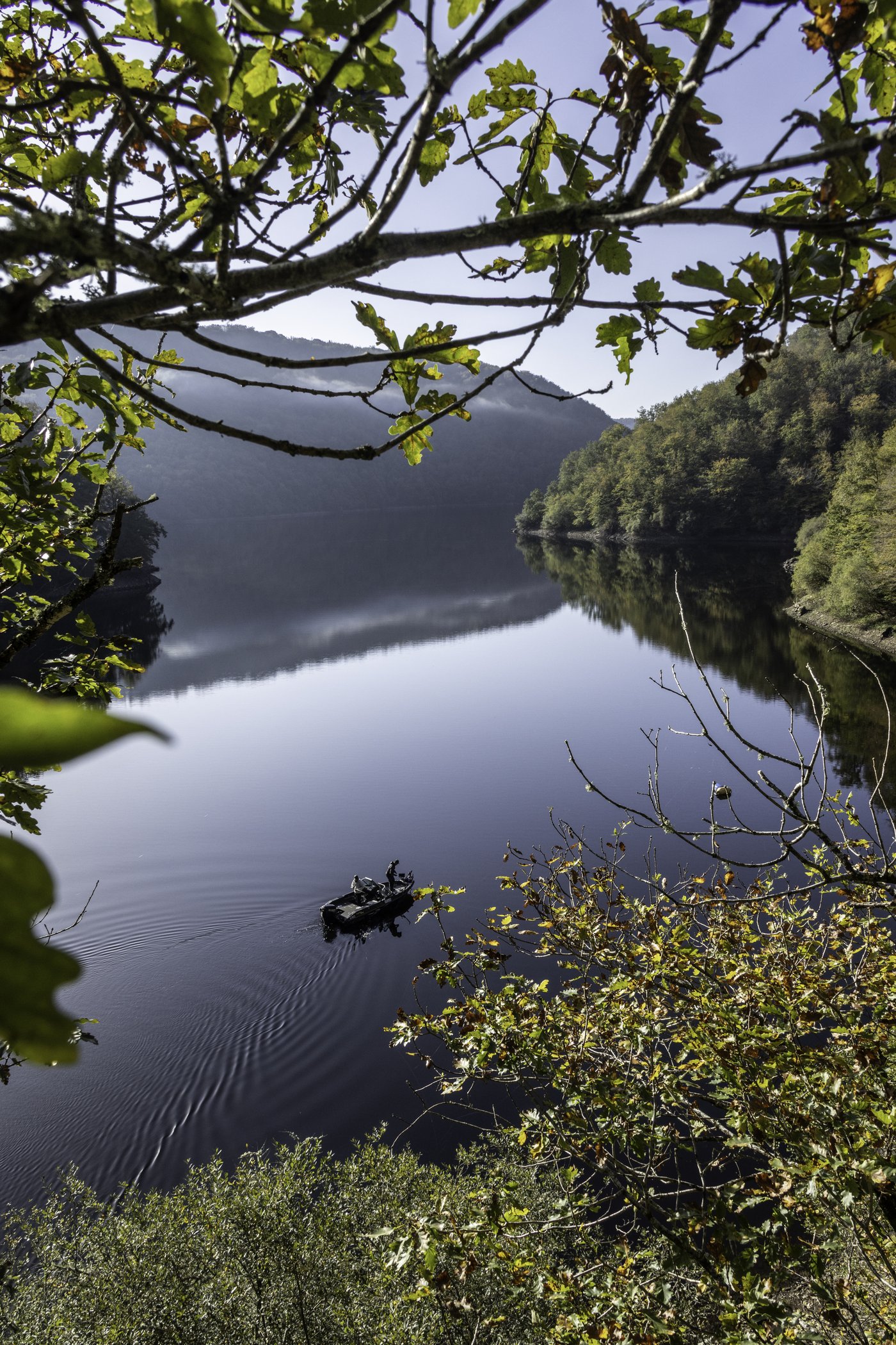 Barque de pêche sur un lac de barrage boisé du Limousin vu depuis la rive