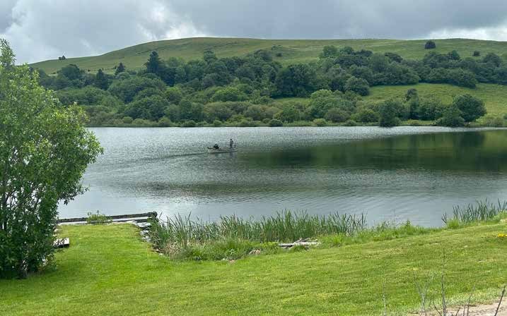 Le lac de Veirières dans le Cantal, entouré de prairies et de hêtres, une barque au loin