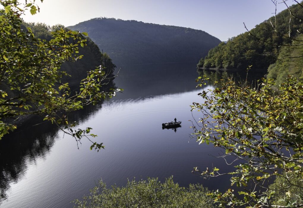 Pêcheur en barque sur un lac de barrage encaissé de Nouvelle-Aquitaine au petit matin