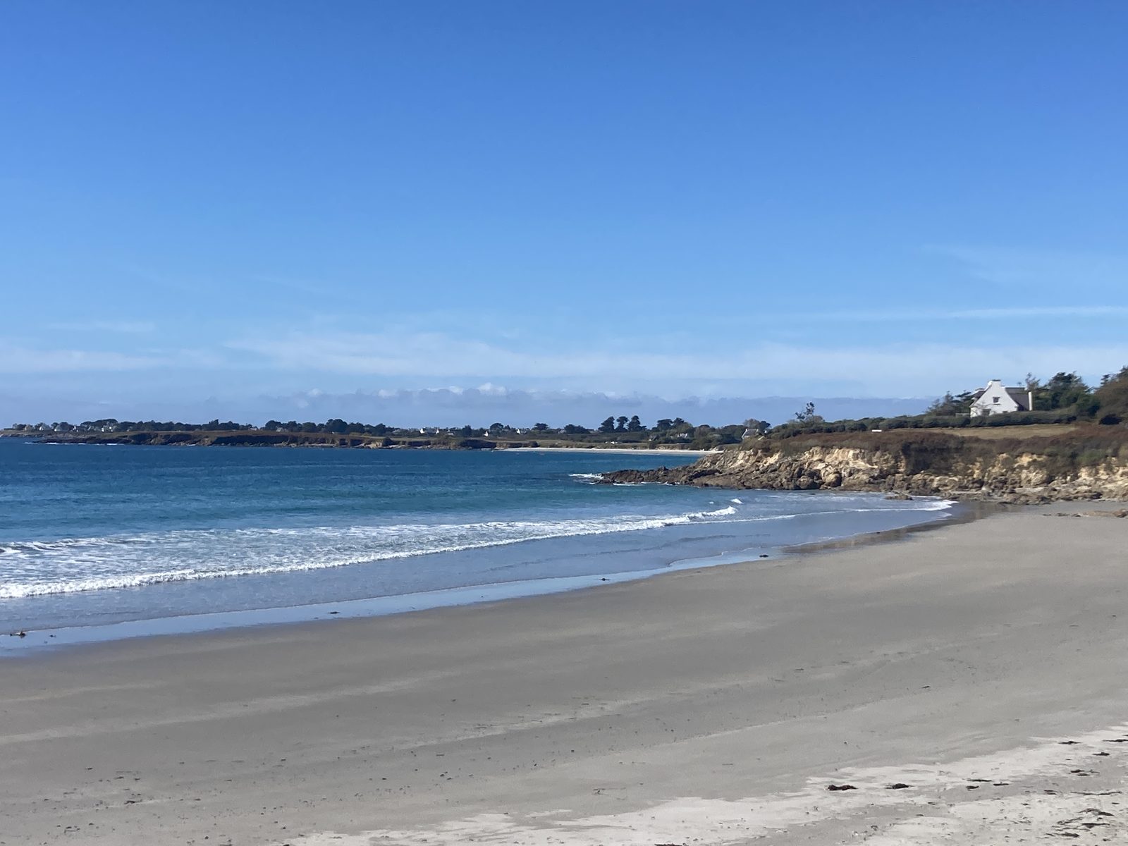 Plage de sable bretonne bordée de rochers, sous un ciel bleu