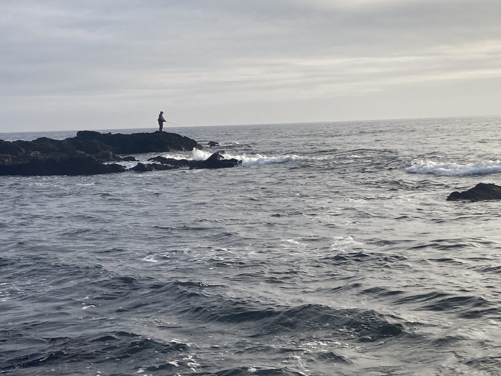 Pêcheur sur une pointe rocheuse battue par la houle, en Bretagne